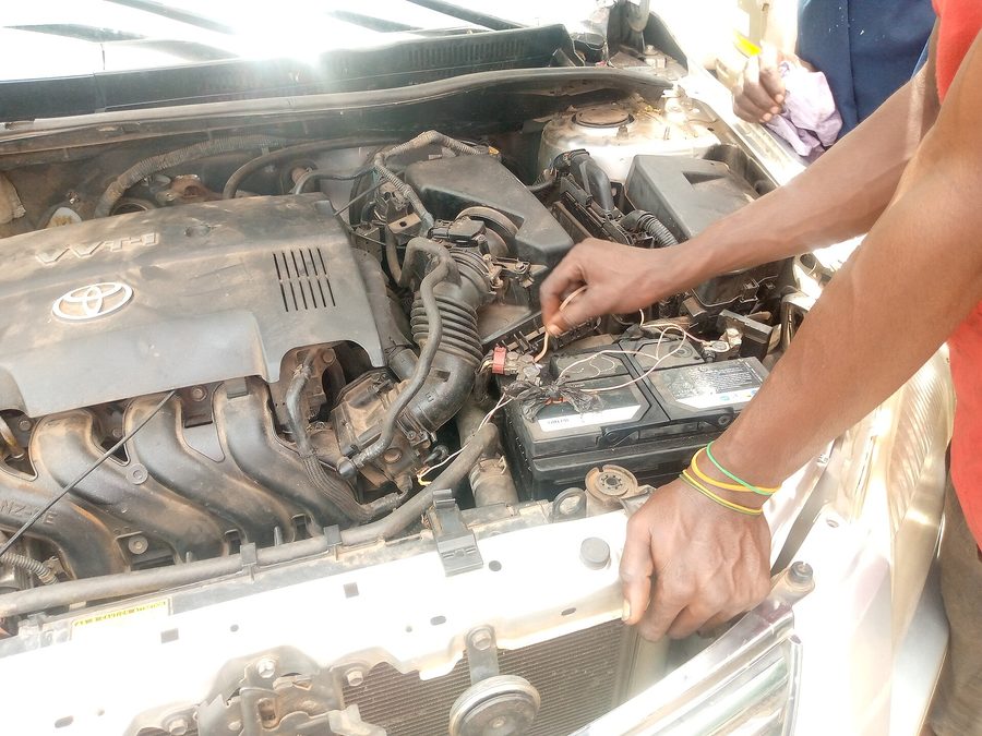 Hands replacing a lead-acid battery in a car engine bay